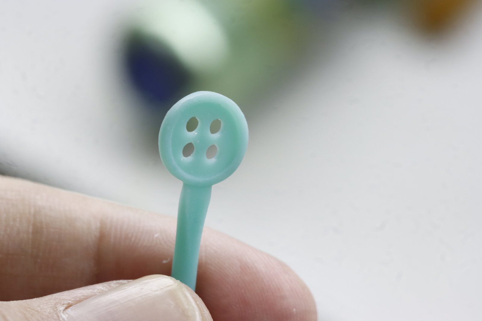 Close-up of a turquoise four-hole jewelry wax model held between fingers during custom jewelry development.