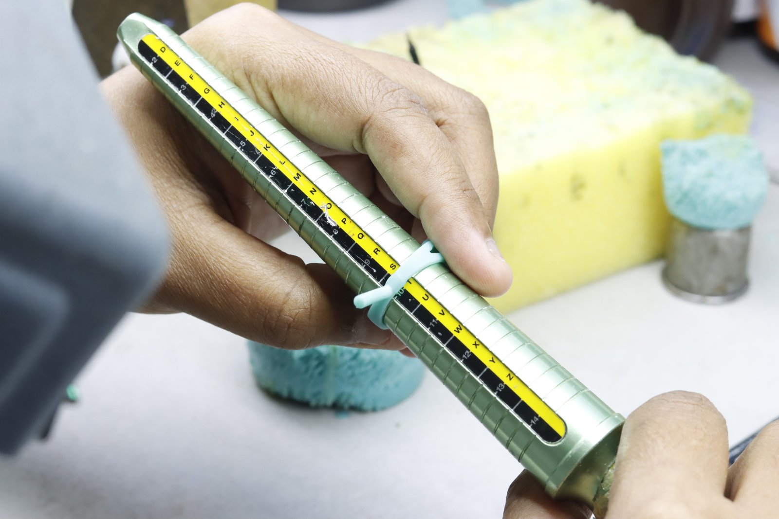 Jewelry manufacturing worker checking the size of a turquoise wax ring model on a graduated ring sizing mandrel during quality control.
